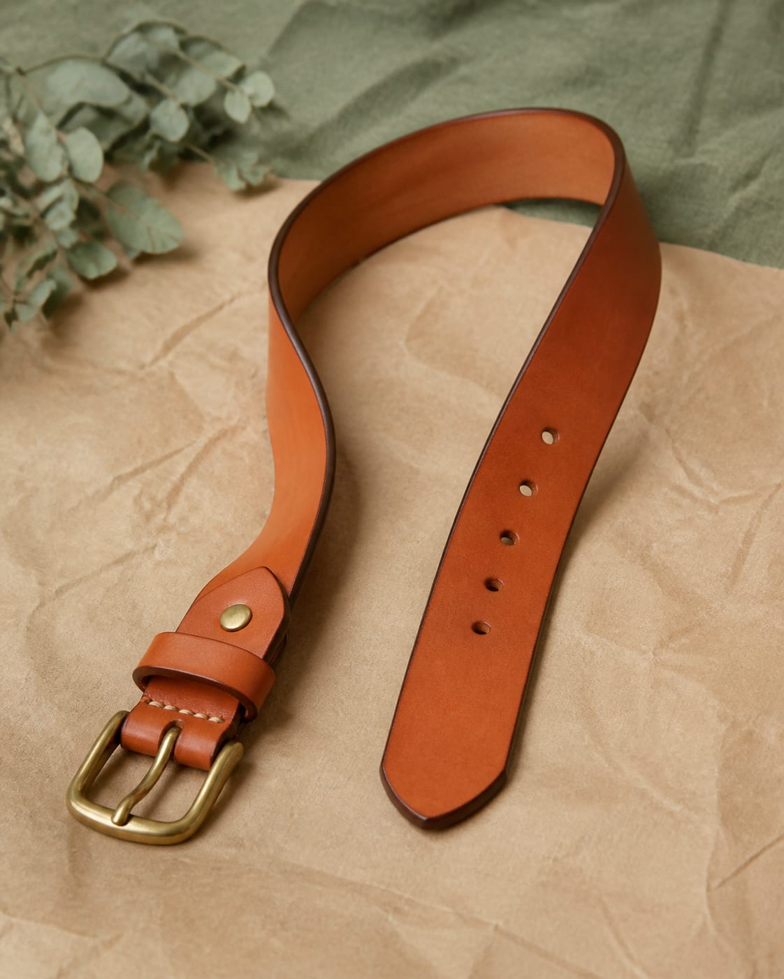 Tan leather belt laid in a gentle curve with antique brass buckle.