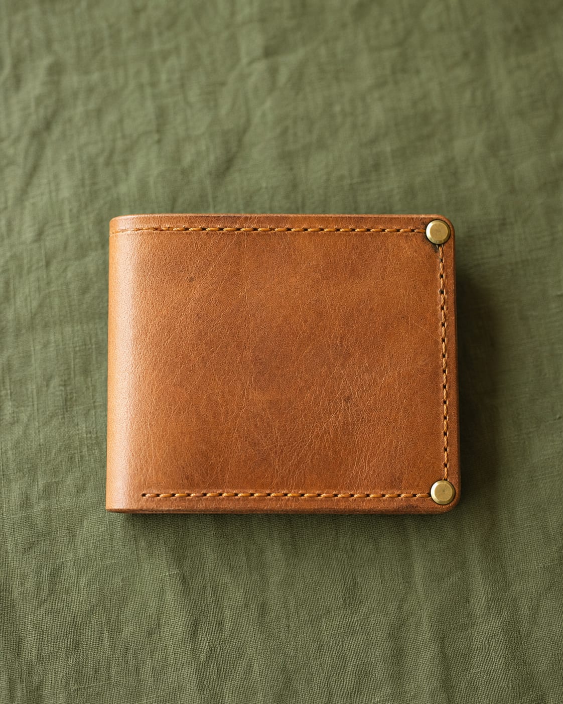 Tan hand-stitched bifold wallet on moss-green linen.