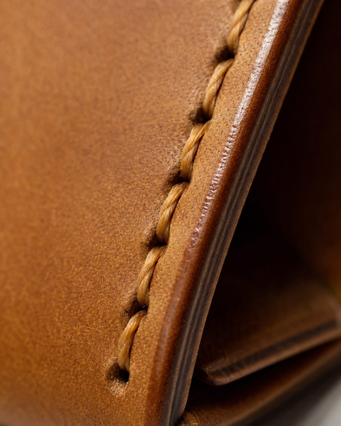 Close-up of saddle stitching and burnished edge on a tan wallet.